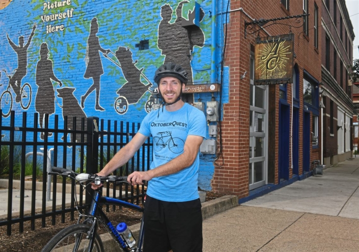 Jesse Descutner, assistant Main Street manager for the Northside Leadership Conference, stops on Foreland Street in Deutschtown near Allegheny City Brewery, on of 14 businesses participating in the We Like Bikes! initiative. (Nate Guidry/Post Gazette)